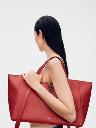 Model holding a large red leather tote bag against a neutral white seamless background