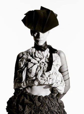 Model Vittoria Ceretti wearing an avant-garde black hat and sculptural textured top against a white seamless background