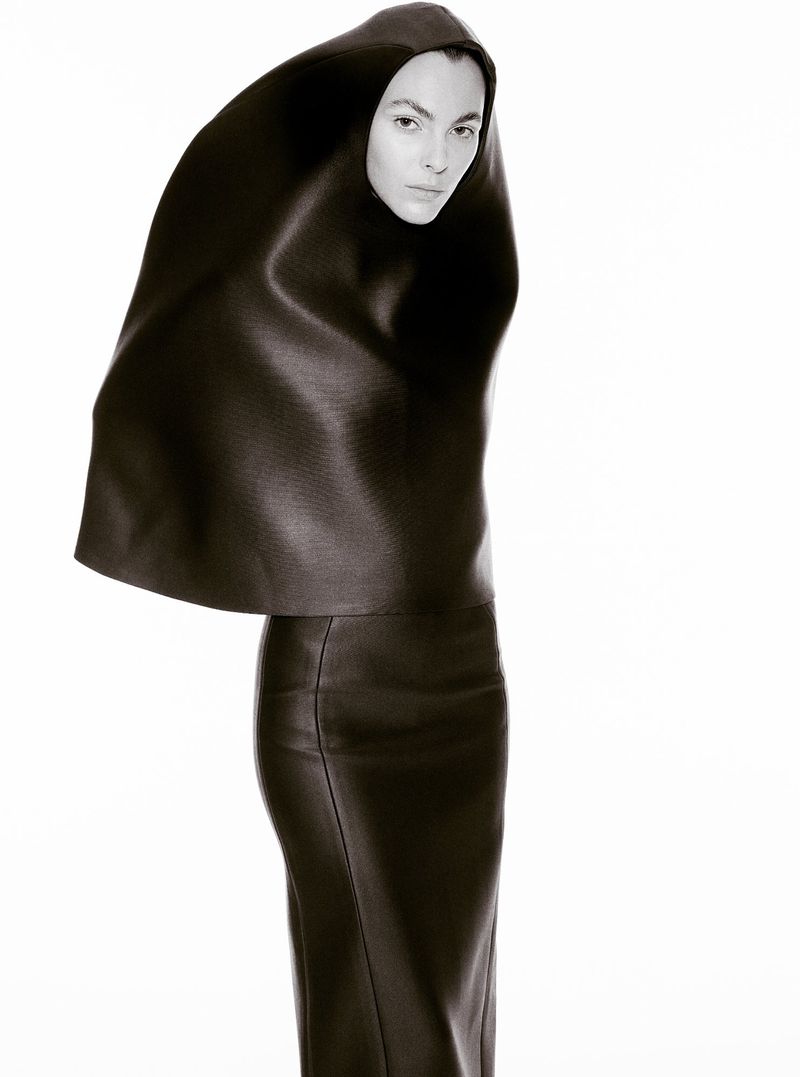 Model Vittoria Ceretti in a sculptural black hooded top and matching skirt against a plain white studio background.