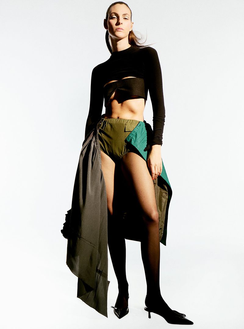 Model Vittoria Ceretti posing in a black crop top and olive layered skirt against a white studio background