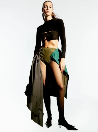 Model Vittoria Ceretti posing in a black crop top and olive layered skirt against a white studio background