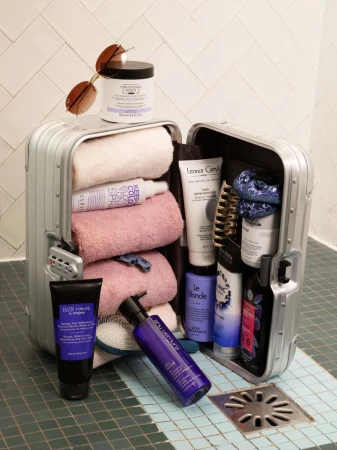Open silver metallic suitcase packed with rolled towels and beauty products resting on green tiled floor