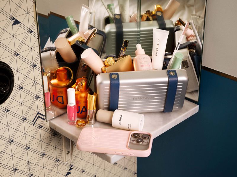 Open silver aluminum vanity case filled with skincare bottles and toiletries on a marble corner shelf with a mirror