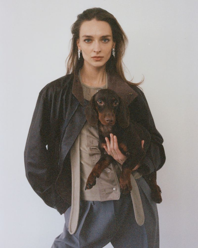 Model Daga Ziober holding a small brown dachshund wearing a dark jacket against a white background