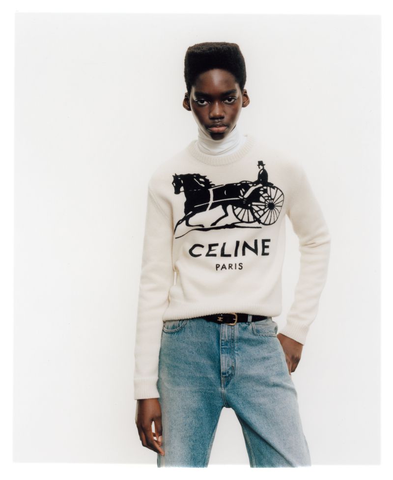 Model wearing a cream graphic sweater and blue jeans against a plain white background