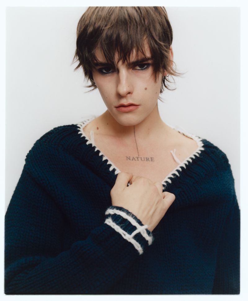 Portrait of a model wearing a dark sweater with white trim against a plain white background for Behind the Blinds.