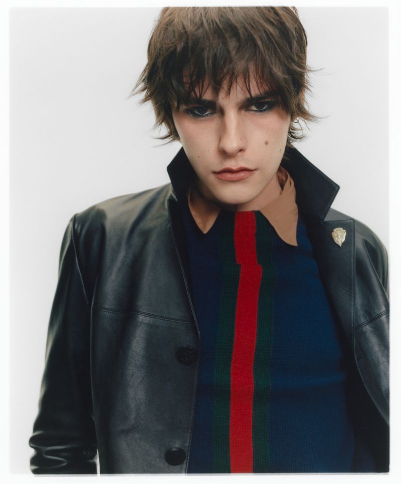 Portrait of a male model wearing a black leather jacket and striped shirt against a plain white background