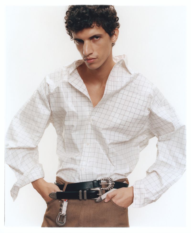 Model in a plaid shirt with hands in pockets against a plain white background