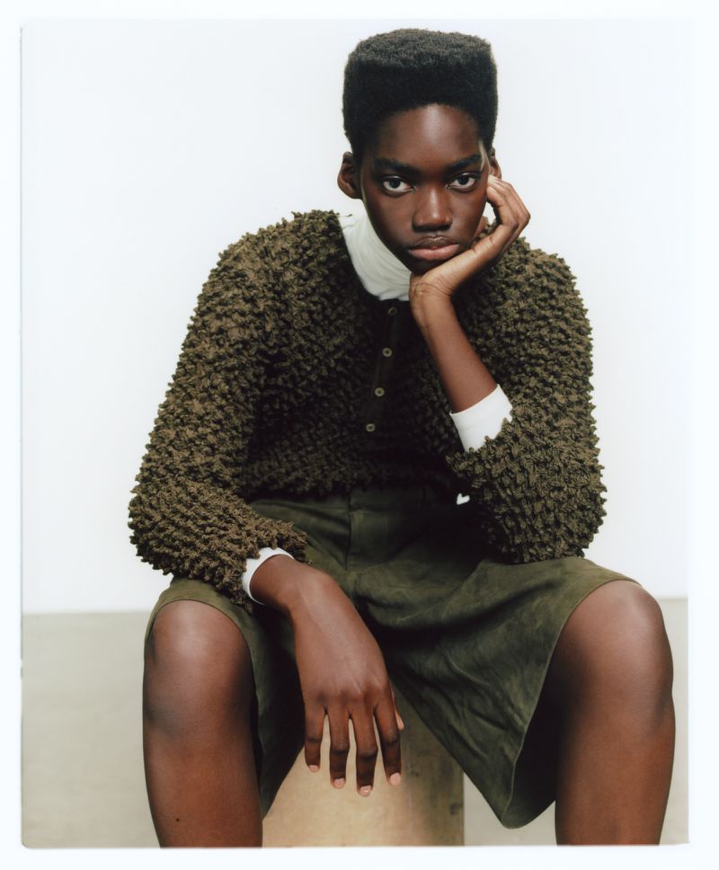 Model with a flat-top haircut wearing a textured olive sweater and matching shorts against a clean white background