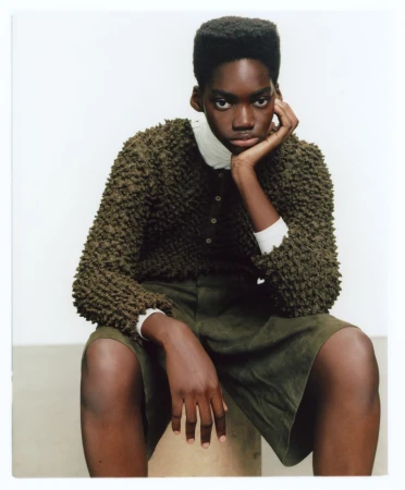 Model with a flat-top haircut wearing a textured olive sweater and matching shorts against a clean white background