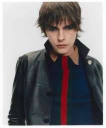 Portrait of a male model wearing a black leather jacket and striped shirt against a plain white background