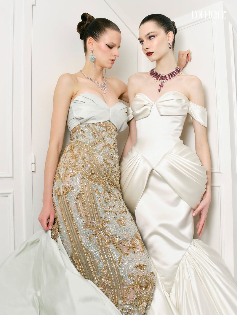 Two female models in couture evening gowns posing against a white door in a high fashion editorial for Haute Tension.