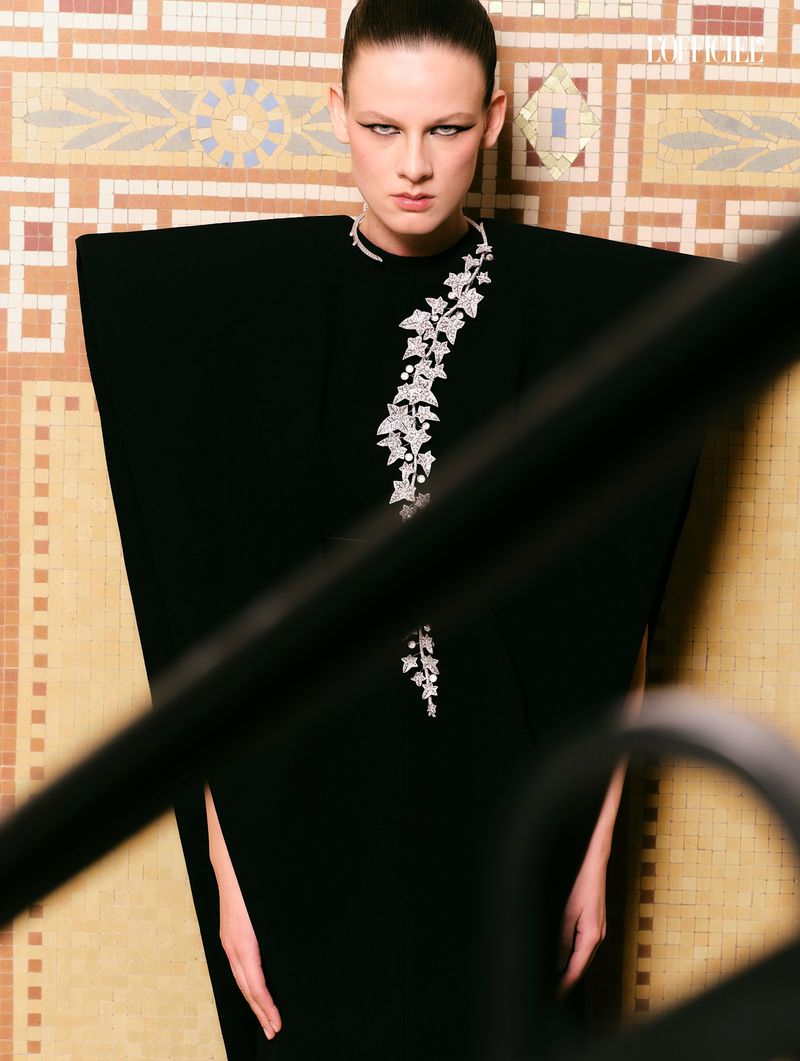 Model in architectural black dress with silver ivy vine detail against a tiled wall
