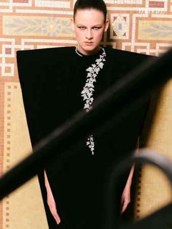 Model in architectural black dress with silver ivy vine detail against a tiled wall