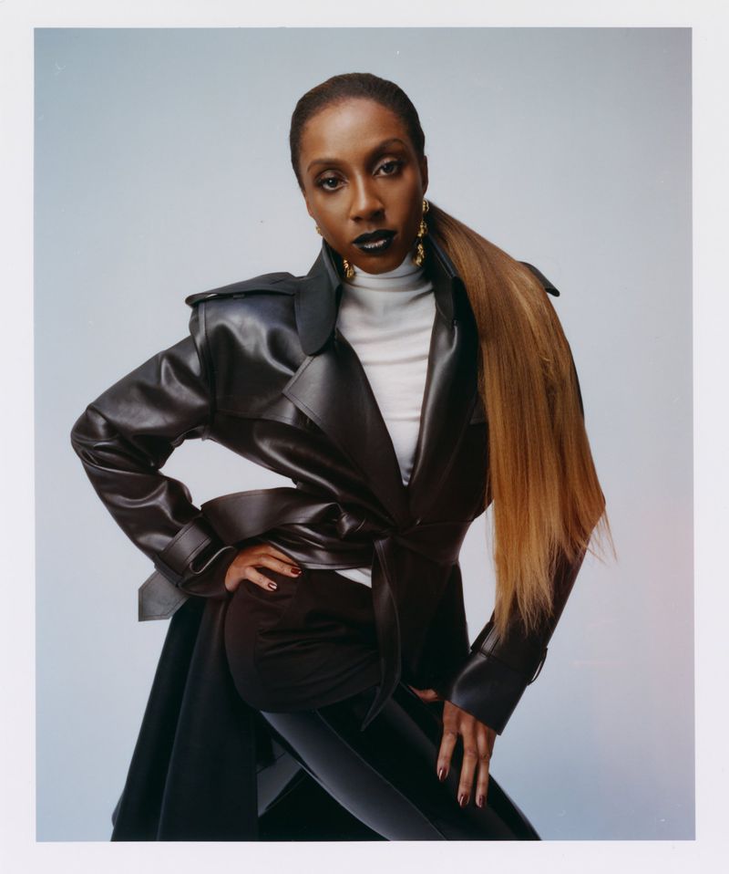 Ziwe Fumudoh in a black leather trench coat over a white turtleneck against a grey seamless background for Love Magazine.