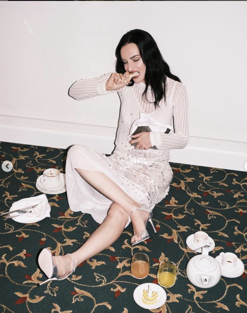 Woman in sheer white dress seated on patterned carpet eating pastry amid teacups and glasses for Marie Claire Italia