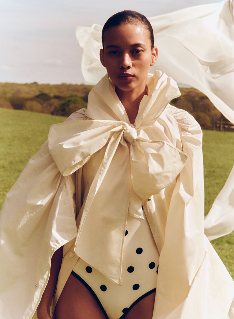 Elegant woman posing in a polka-dot swimsuit and oversized bow dress in a field, fashion editorial, outdoor photoshoot in nature.
