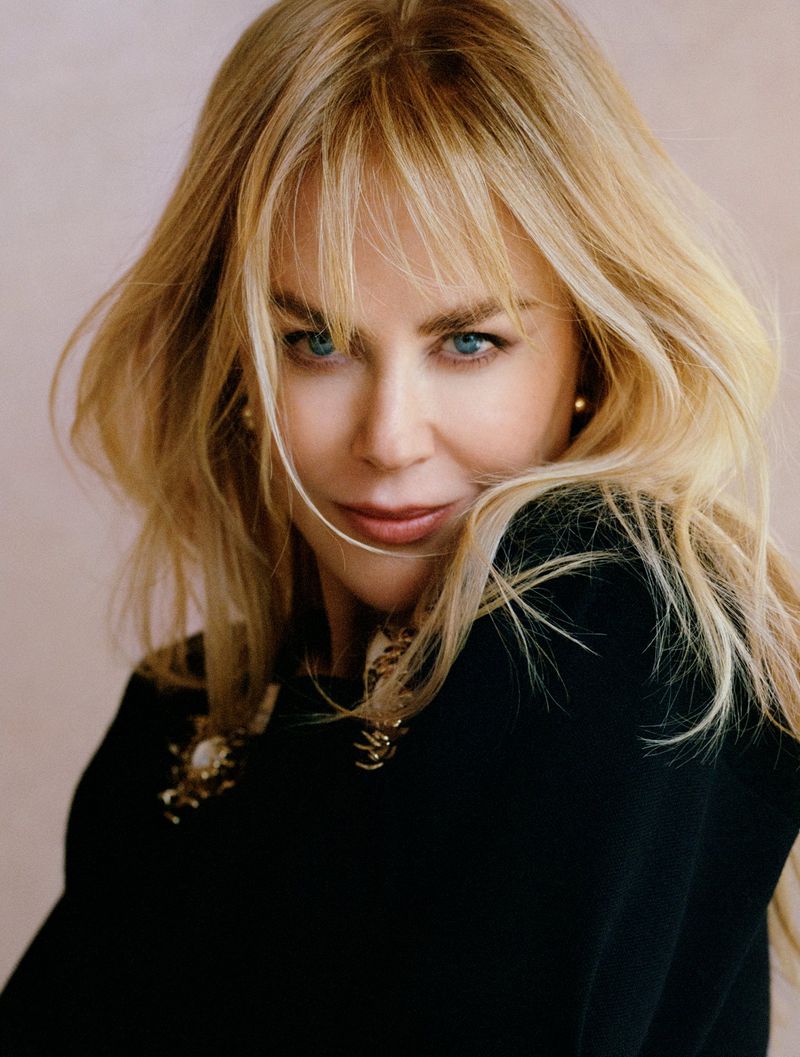 Close-up portrait of Nicole Kidman with blonde hair and blue eyes wearing a black top against a neutral background.