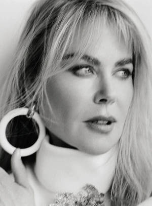 Close up portrait of a blonde woman wearing a large round earring and high neck collar against a white background