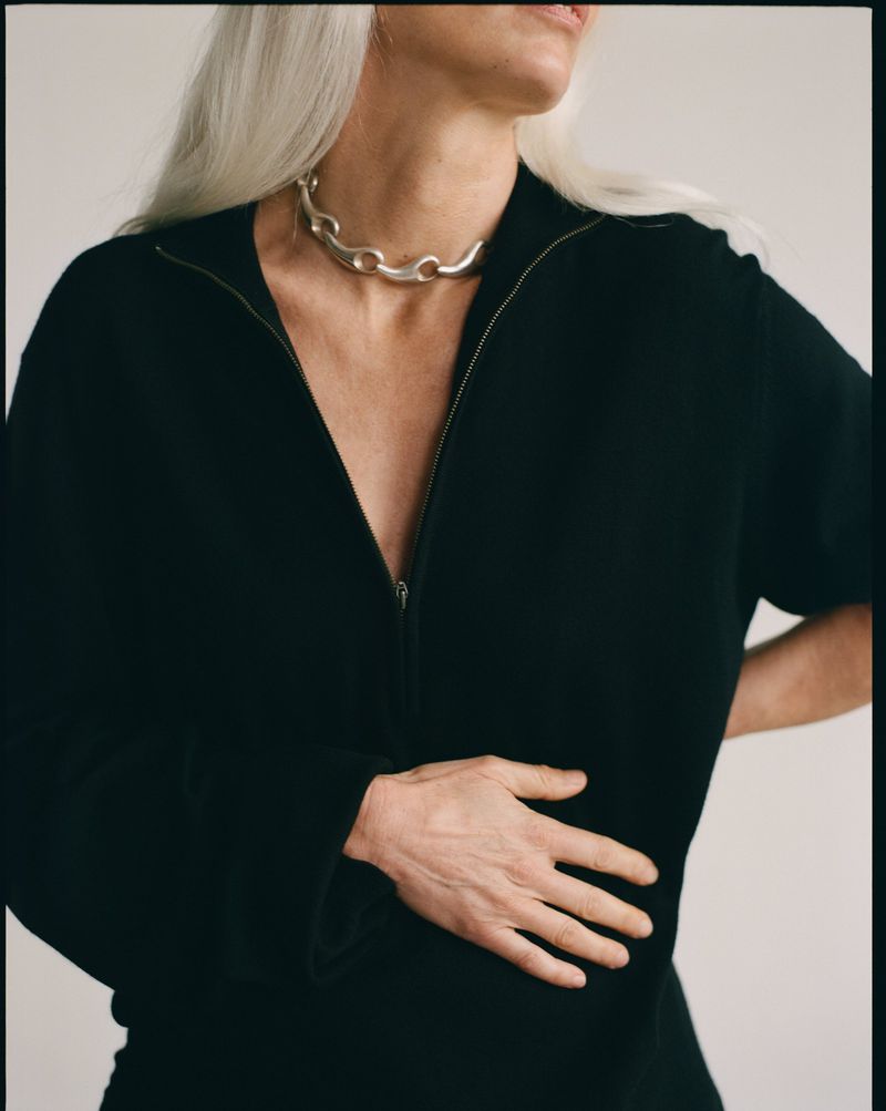 Cropped portrait of an adult woman in a black shirt and silver chain necklace against a neutral background in a studio setting.