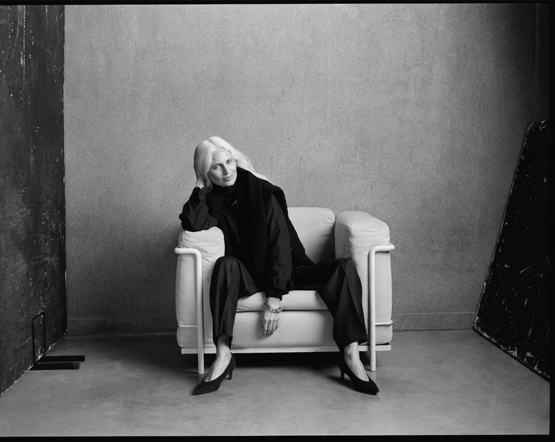 Model seated in an armchair against a textured studio wall in a black and white portrait for P. Johnson Femme Fall 26.