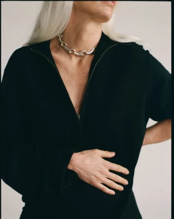 Model wearing a black zip-up top and a chunky silver choker necklace against a neutral wall background.