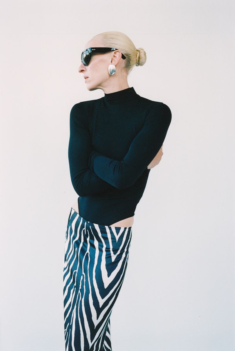 Model wearing black long sleeve top and zebra print skirt with dark sunglasses against white background