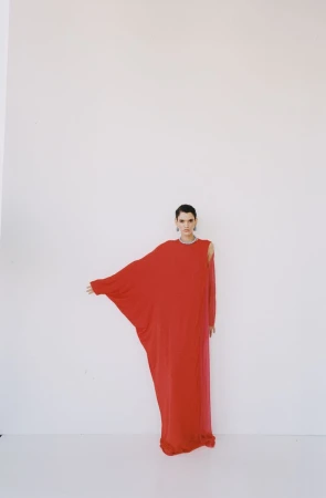 Model wearing a flowing red dress standing against a plain white studio backdrop for The New Arrivals project.
