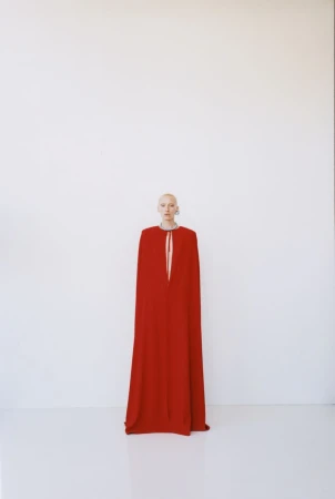 Model wearing a long red cape gown standing against a plain white background for The New Arrivals lookbook project