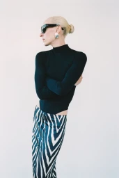 Model wearing black long sleeve top and zebra print skirt with dark sunglasses against white background