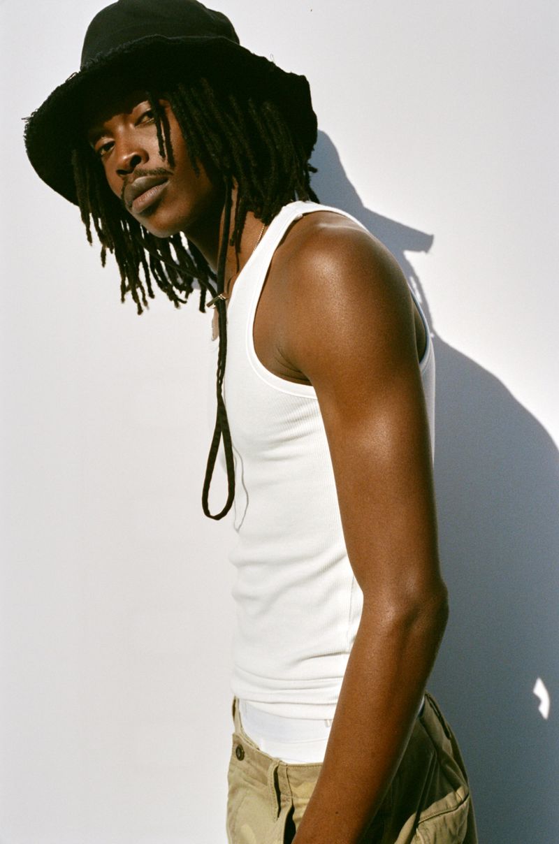 Model wearing a white tank top and black bucket hat against a plain white studio background for Gap Spring 2026.