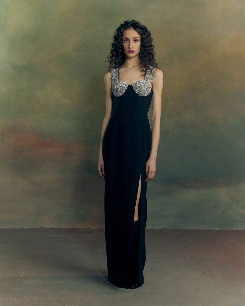 Model standing in a long black dress with embellished bustier against a painterly backdrop for Patrick McDowell AW26 Lookbook