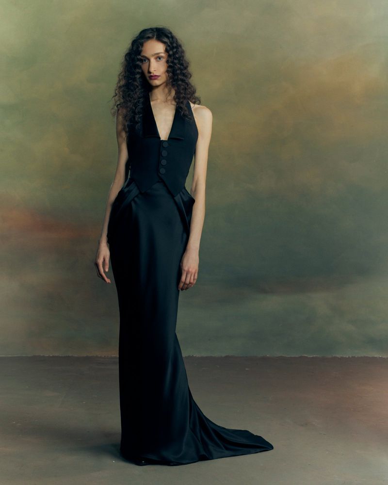 Model with long curly hair wearing a black sleeveless vest gown in a moody studio portrait for Patrick McDowell AW26