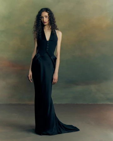 Model with long curly hair wearing a black sleeveless vest gown in a moody studio portrait for Patrick McDowell AW26