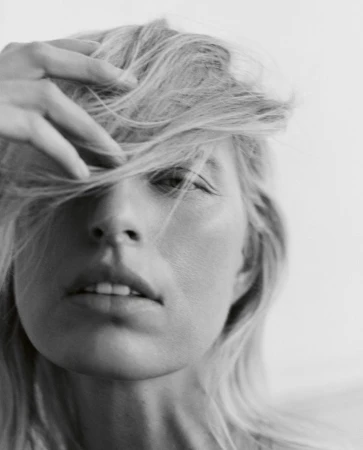 Close-up portrait of model Karolina Kurkova with blonde hair across her face against a plain background