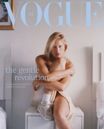 Model Karolina Kurkova seated on a white nightstand wearing white socks and sneakers against a bedroom background