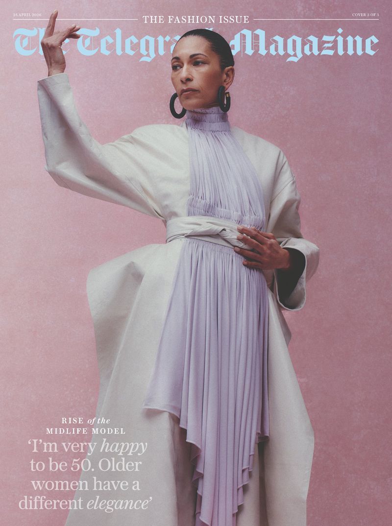 Model Noemie Lenoir wearing an off-white coat and pleated lilac dress against a pink textured background.