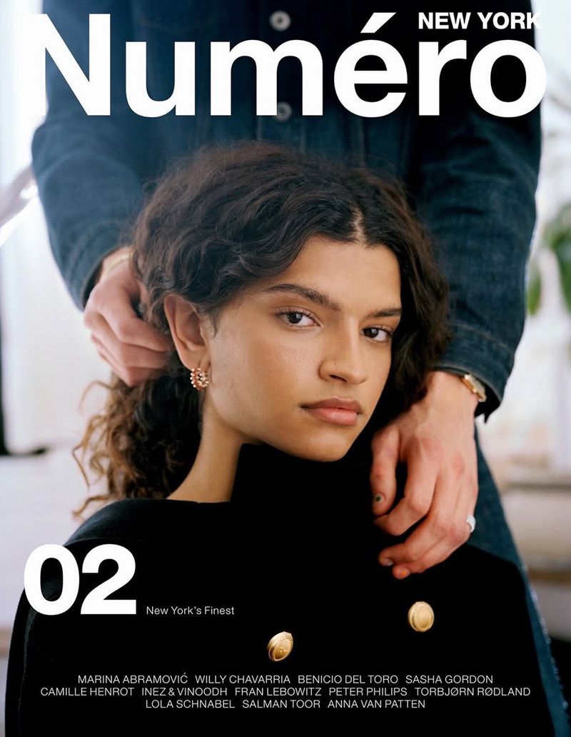 Magazine cover featuring a young woman in a black jacket, photographed in a medium shot with a pair of hands adjusting her collar.