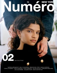 Model with dark curly hair posing in a black coat with gold buttons, framed by a person in a denim jacket