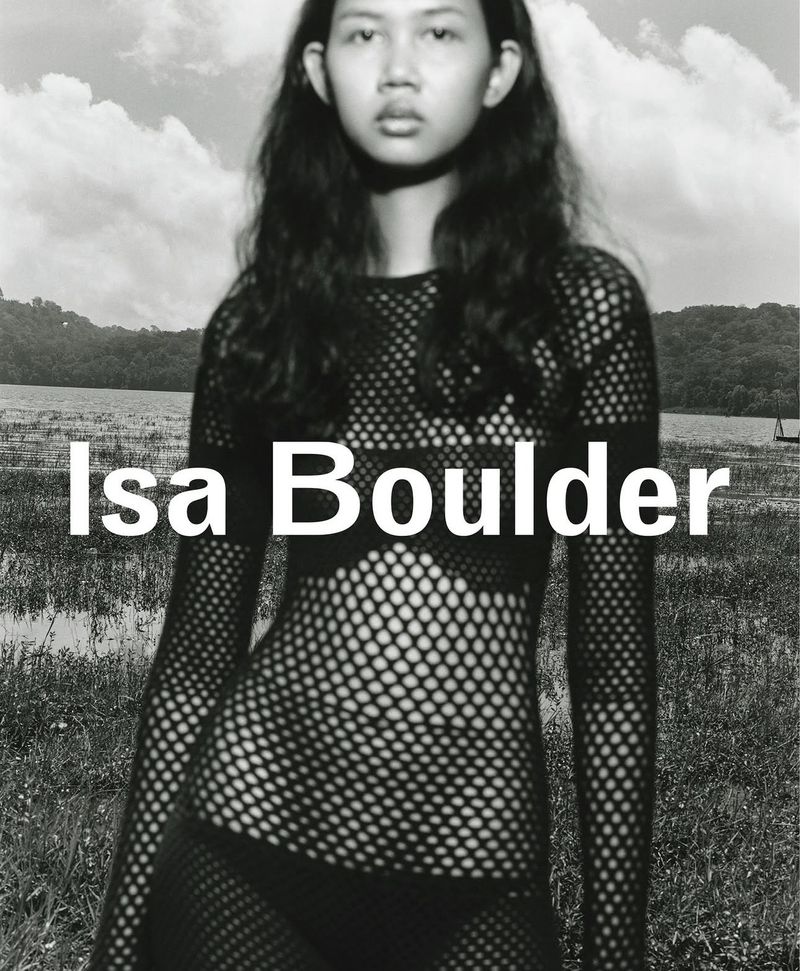 Model wearing a black fishnet top outdoors against a lake and cloudy sky for the Isa Boulder spring summer campaign.