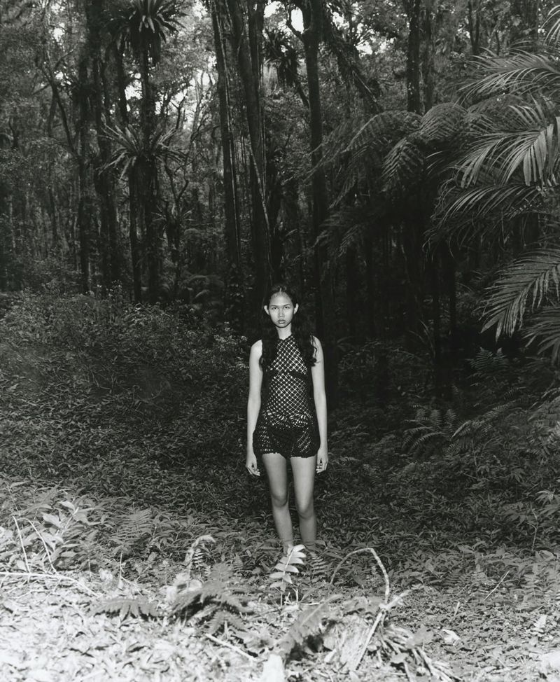 Model wearing a black knit dress standing on a path in a dense green forest