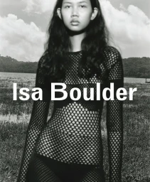 Model wearing a black fishnet top outdoors against a lake and cloudy sky for the Isa Boulder spring summer campaign.