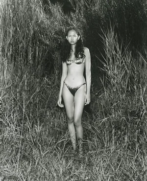 Model standing in tall marsh grass wearing a patterned two-piece swimsuit in a black and white fashion editorial photograph.