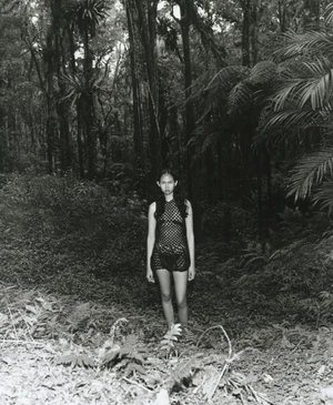 Model wearing a black knit dress standing on a path in a dense green forest