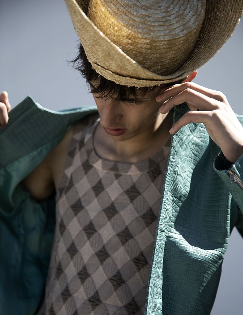 Model wearing a straw hat and textured teal jacket over a checked tank top, photographed by Karl Simone for L'Officiel Hommes Malaysia.