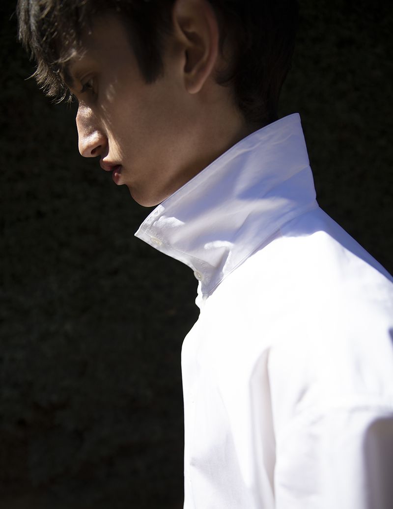 Close-up profile portrait of Nicolas Secades wearing a crisp white shirt with an upturned collar against a dark background