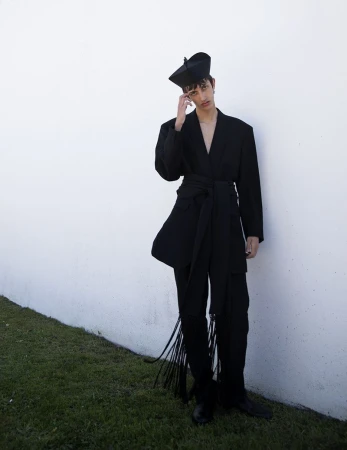 Model Nicolas Secades in a black suit with a brimless hat posing against a white wall for L'Officiel Hommes Malaysia.