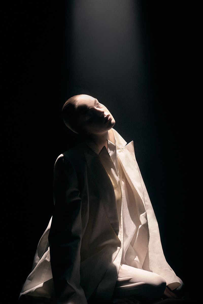 Model in white blazer under a dramatic overhead spotlight against a dark background for Numéro Switzerland editorial