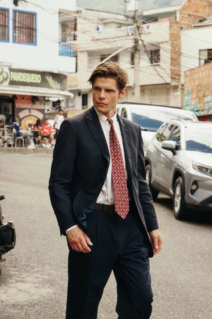 Model Alessandro Egger wearing a dark suit and patterned tie walking on a sunny city street for L'Officiel Ukraine