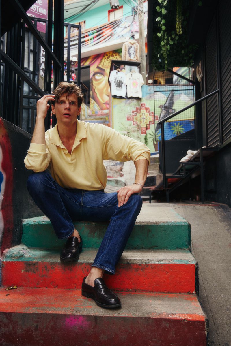 Alessandro Egger wearing a yellow polo shirt and jeans seated on colourful outdoor stairs for L'Officiel Ukraine